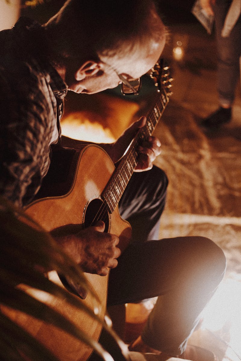 Man playing acoustic guitar by firelight creating a cozy atmosphere.